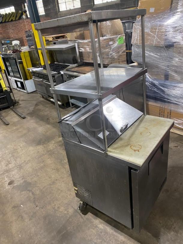 True stainless steel single door refrigerated prep table, model TSSU-27-08. Features double overhead shelf, cutting board, and wire rack. On casters.