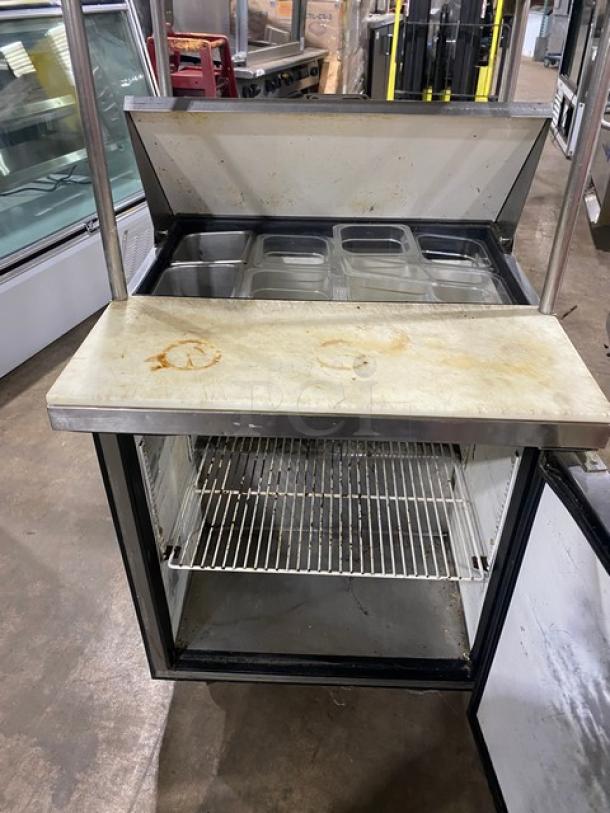 True TSSU-27-08 refrigerated prep table, single door, stainless steel, double overhead shelf, cutting board, wire rack, on casters.