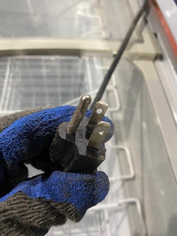 Plug of an Excelente CF-289 commercial chest freezer. 115V, shown with gloved hand for size reference.
