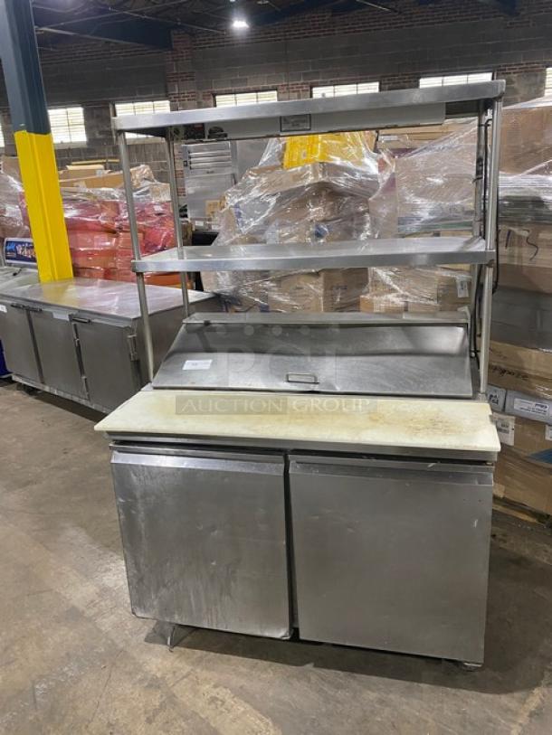 Commercial stainless steel refrigerated prep table with double overhead shelf, Hatco strip warmer, and casters.