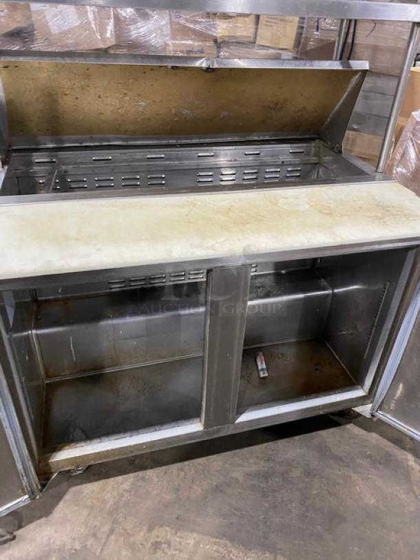 Commercial stainless steel 2-door refrigerated prep table with bain marie style. Features double overhead shelf, Hatco strip warmer, and casters.