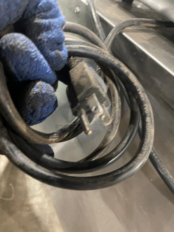 Coiled electric cord of FWE Commercial Stainless Steel Heated Cabinet, Model HLC-SL1826-8-CHP, 120V, seen with blue-gloved hand.