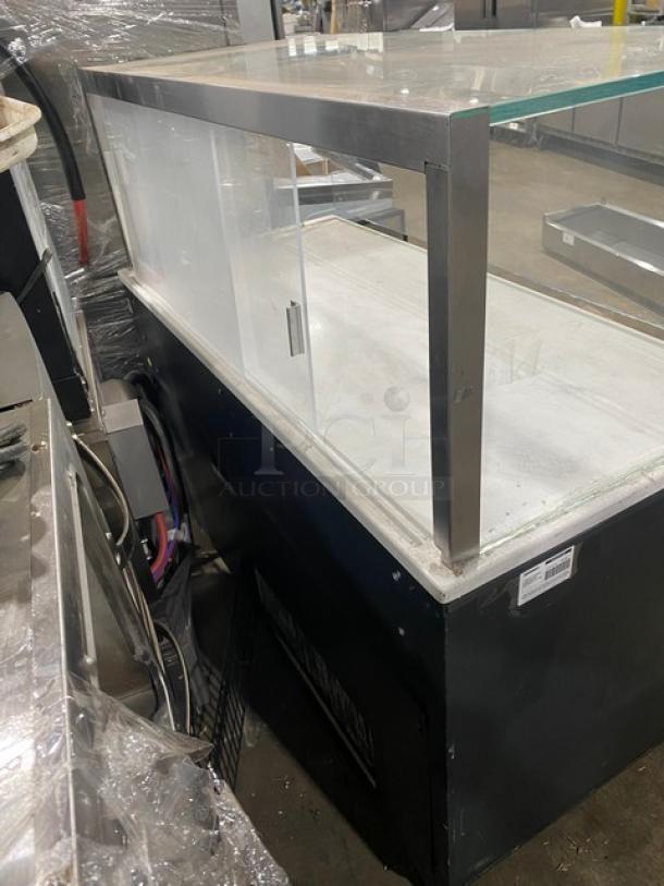 Commercial black refrigerated display case with glass showcase, multi-level shelving, on legs. Ideal for grab-n-go setup.