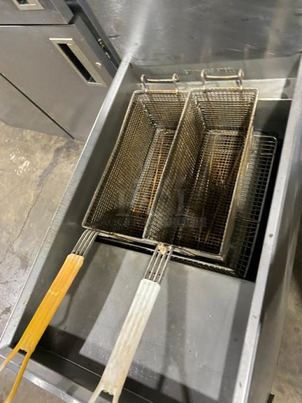 Imperial stainless steel natural gas deep fat fryer with backsplash, includes two fry baskets, on sturdy legs. Slight wear visible.