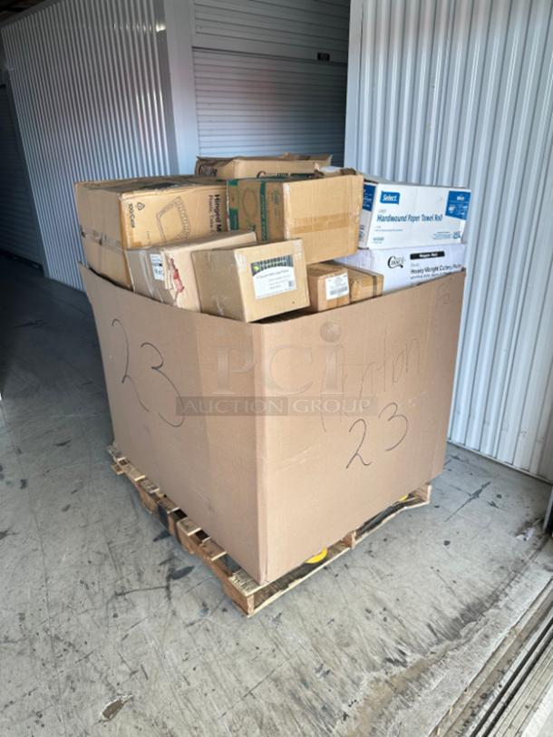 Mixed pallet of boxed items including paper towels and cutlery packs, labeled "Auction 23" on a wooden pallet.
