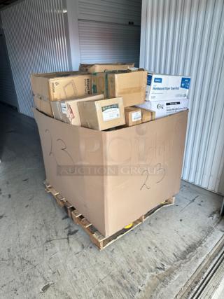 Mixed pallet of boxed items including paper towels and cutlery packs, labeled "Auction 23" on a wooden pallet.