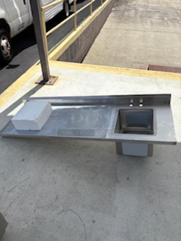 Brand new Regency one compartment sink with left drainboard, stainless steel, visible scratch and dent, outdoors on pavement.
