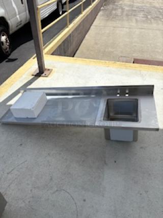 Brand new Regency one compartment sink with left drainboard, stainless steel, visible scratch and dent, outdoors on pavement.