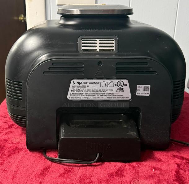 Ninja FG551 Foodi Smart XL indoor grill, 6-in-1, black, back view showing model and safety label, on red cloth.