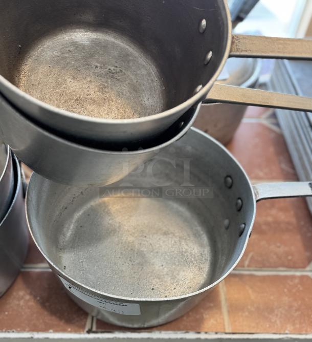 Three assorted saucepans with handles, showing wear and use, set on a tiled surface. Visible label indicates "3 x Bid."