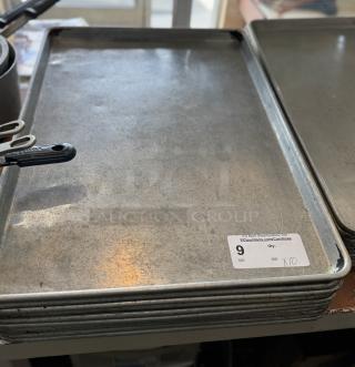 Stack of large sheet pans, slightly worn, auction tag indicates quantity of 10. Ideal for baking or commercial use.