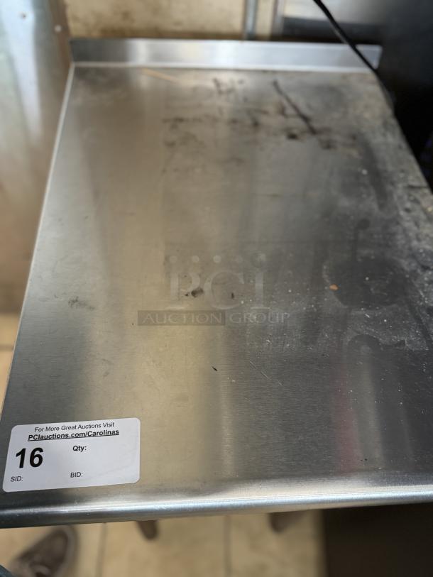 Stainless steel work table with visible wear and scratches, auction tag number 16, promoting PCauctions.com/Carolinas.