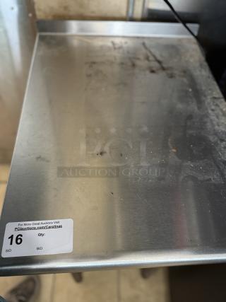 Stainless steel work table with visible wear and scratches, auction tag number 16, promoting PCauctions.com/Carolinas.