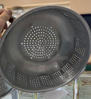 Large aluminum colander with a perforated design, showing light wear. Ideal for straining and washing.