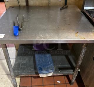 Stainless steel work table with tubular legs, used condition, shows stains and wear, includes lower storage shelf.