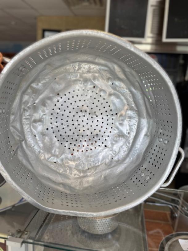 Large aluminum colander with perforated design, dual handles, and used condition. Ideal for draining pasta and vegetables.