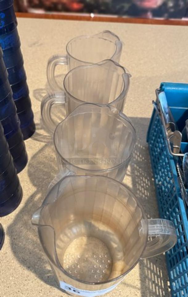 Four 64 oz. clear plastic pitchers, used condition, lined up on a counter. Perfect for drinks and catering services.