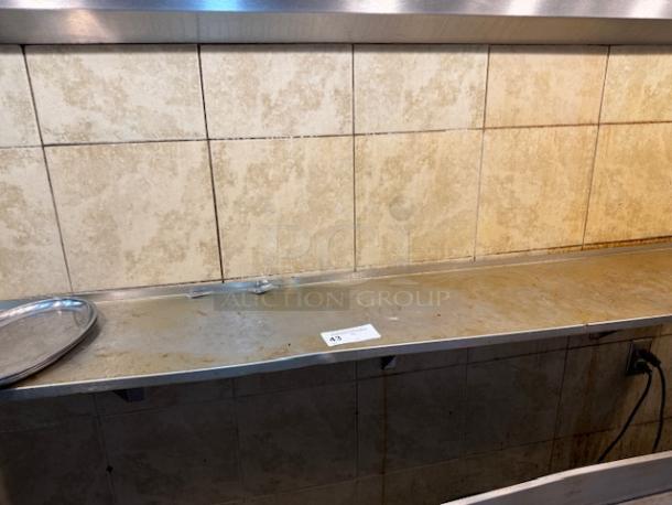72" stainless steel wall shelf with a slight patina, mounted against beige tile wall. Includes auction tag number 43.