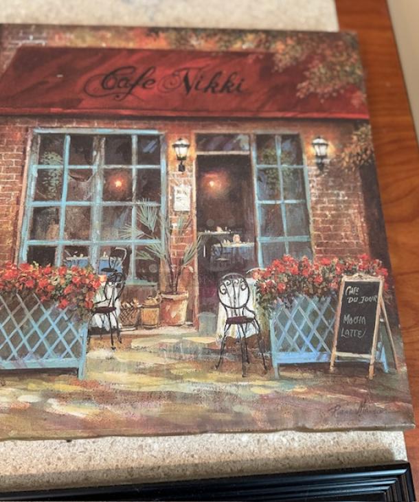 Italian artwork titled "Cafe Nikki," depicting a charming cafe scene with vibrant flowers and vintage chairs, signed by the artist.