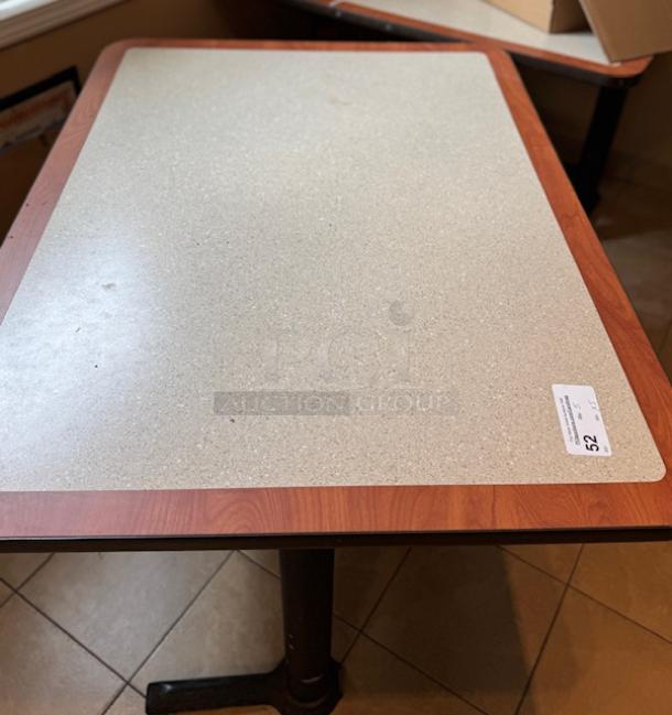 Rectangular dining room table with wood trim, light beige surface, and pedestal base. Tag shows lot number 52.