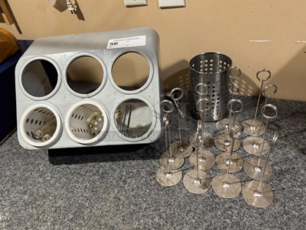Metal utensil holder and multiple metal table number holders on a countertop. Utensil holder has five circular slots.