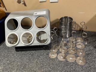Metal utensil holder and multiple metal table number holders on a countertop. Utensil holder has five circular slots.