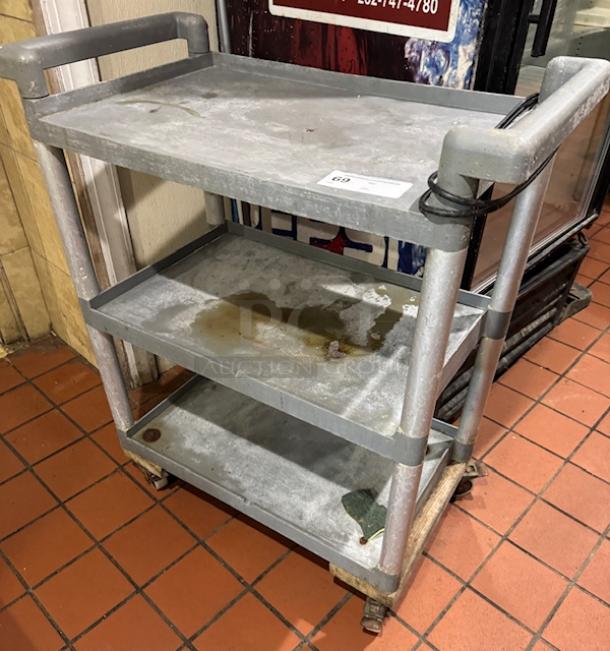 Three-tier gray bus cart on casters, showing wear and stains. Includes a handle and protective edges, with a visible tag.