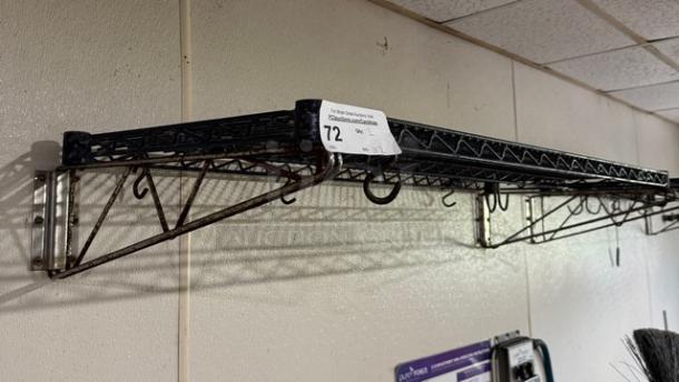 Wire wall shelving unit with metal frame and hooks, marked with sticker "72," mounted on wall, moderate wear.