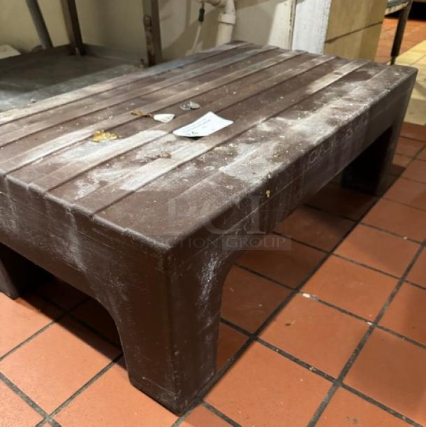 Brown plastic dunnage rack with slatted top, showing signs of wear. Ideal for storage. Tags indicate model and specs.