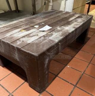 Brown plastic dunnage rack with slatted top, showing signs of wear. Ideal for storage. Tags indicate model and specs.
