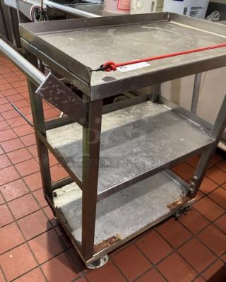 Metal bus cart on casters with three shelves, sturdy steel construction, visible wear, suitable for kitchen use.