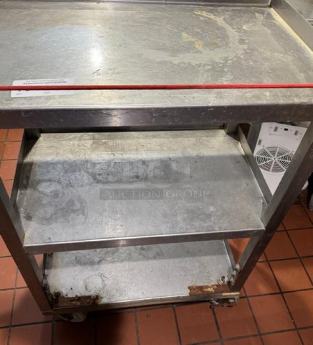 Metal bus cart on casters, three-tier shelves, stainless steel, visible wear and scratches, ideal for restaurant use.