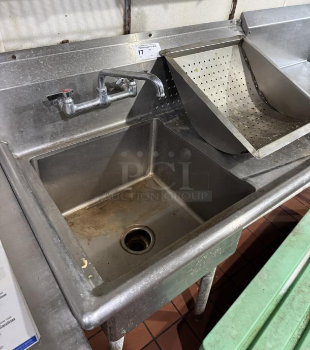 Stainless steel 1 compartment sink with attached drain board and built-in strainer, featuring wall-mounted faucet.
