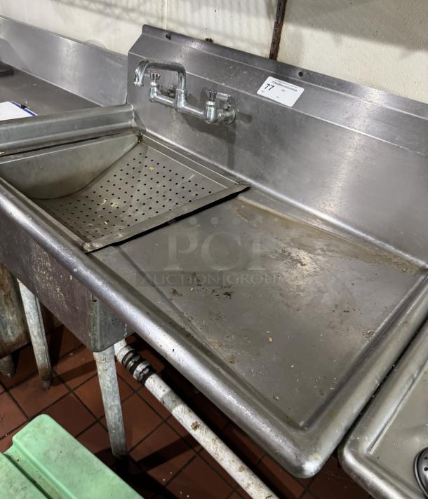 Stainless steel 1 compartment sink with drain board and built-in strainer. Visible faucet, worn condition, suitable for commercial use.