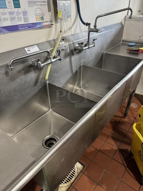 3 compartment stainless steel sink with 2 drain boards, commercial use, clean condition, visible water lines and faucets.
