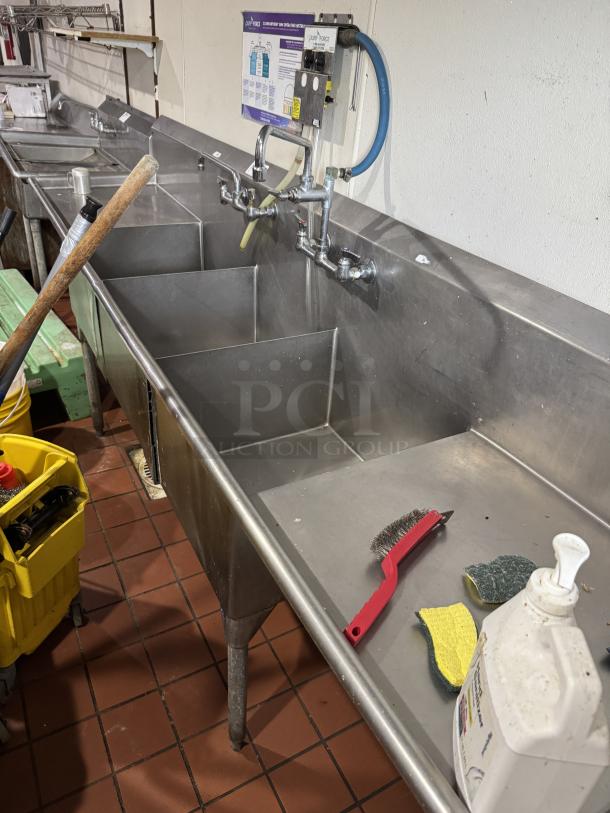 Stainless steel 3 compartment sink with 2 drain boards, equipped with faucet and sprayer system, in good condition.