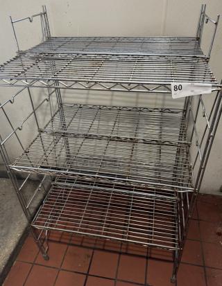 Metal floor rack with four wire shelves, silver finish, slight wear visible. Auction tag "80" attached. Ideal for storage.