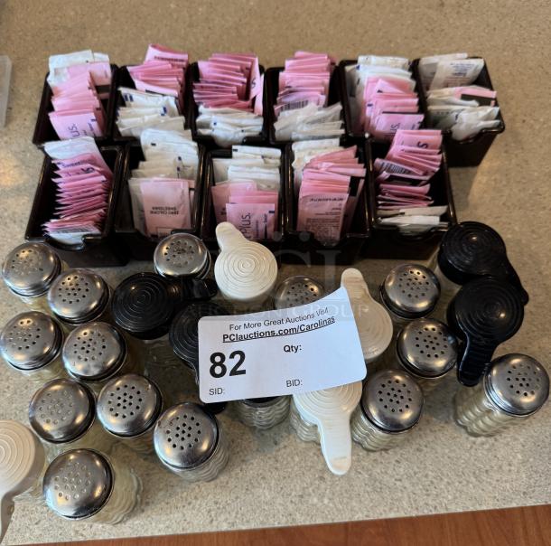 Assorted salt and pepper shakers, metal lids; sugar packet holders filled with sweetener packets; auction lot number 82.