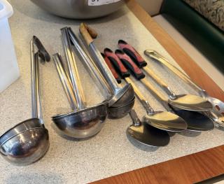 Assorted metal spoons and ladles, 11-piece set, various sizes, with wooden and plastic handles, on countertop.