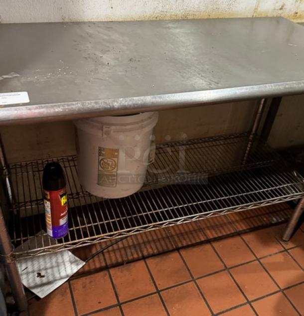 Stainless steel work table with wire undershelf, surface stains, sturdy design, ideal for kitchen or industrial use.