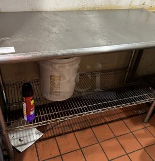 Stainless steel work table with wire undershelf, surface stains, sturdy design, ideal for kitchen or industrial use.