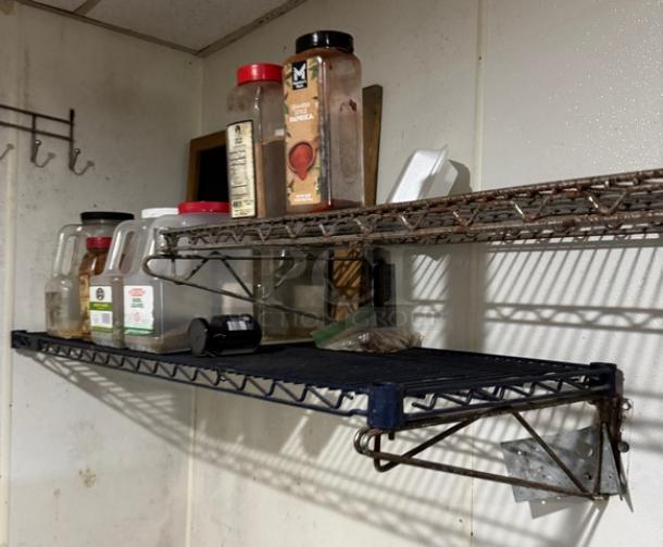 Wall-mounted wire shelving with spices, metal racks, signs of wear. Two-tiered shelves in a kitchen setting.