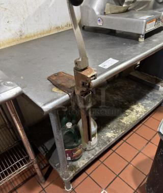 Stainless work table with under shelf and attached #10 can opener. Visible wear and rust; includes slicer machine.
