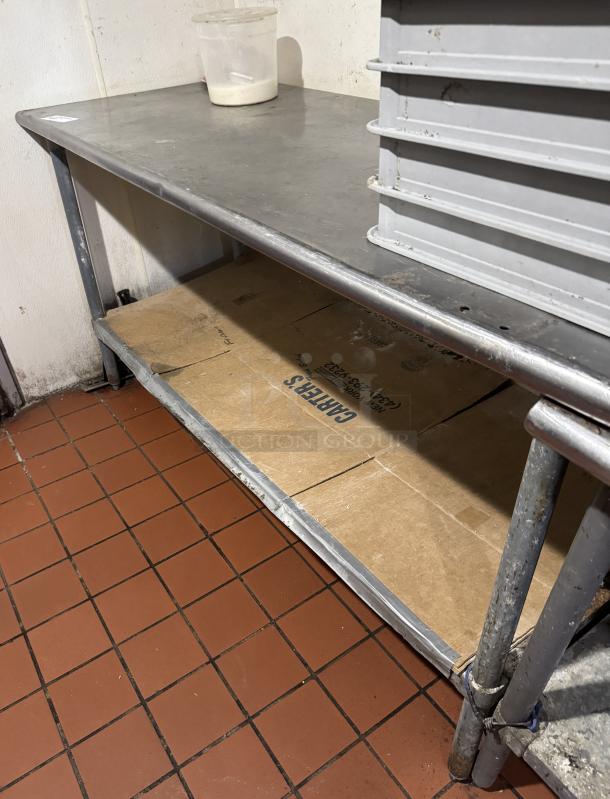 Stainless steel work table with under shelf, visible wear, sturdy construction; ideal for kitchen use or storage spaces.