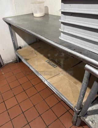 Stainless steel work table with under shelf, visible wear, sturdy construction; ideal for kitchen use or storage spaces.
