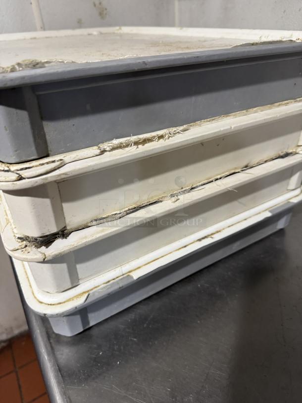 Four stacked dough pans with lids, worn edges, used condition, ideal for baking, shown on a metal surface.