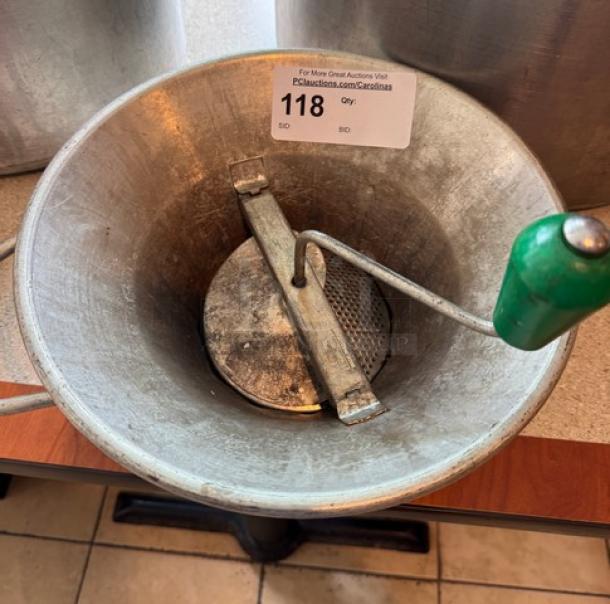 Vintage metal ricer with green handle, perforated base, and visible patina. Auction tag indicates item number 118.