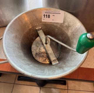 Vintage metal ricer with green handle, perforated base, and visible patina. Auction tag indicates item number 118.