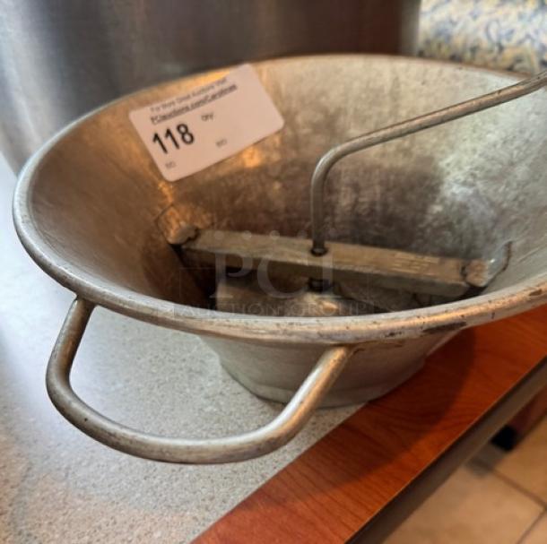 Metal ricer with two handles and rotating mechanism, item tag number 118 attached, showing surface wear.