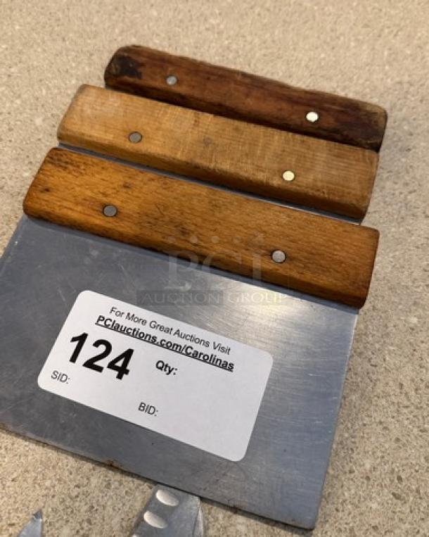 Assorted knives and dough scrapers with wooden handles on display. Features a label for auction item 124.